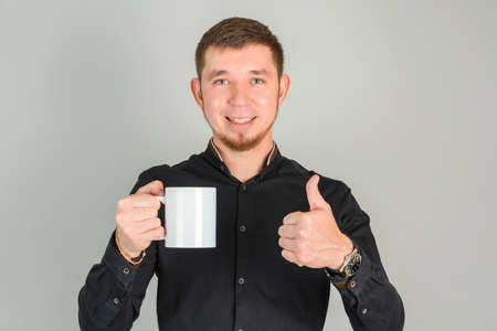 A smiling bearded man holds a large white cup in his hands and shows a thumbs up gesture while...