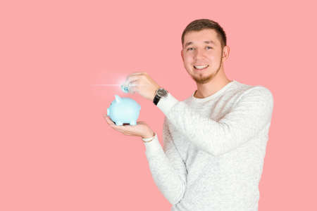 A male investor puts a silver bitcoin coin in a blue piggy bank standing on a pink background, copyspaceの写真素材