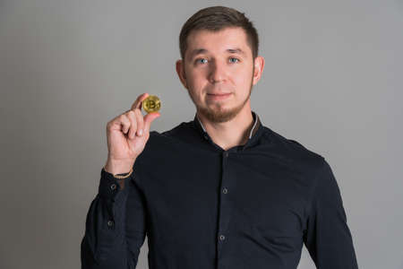 Bearded hipster holding btc gold coin in hand while standing on gray backgroundの写真素材