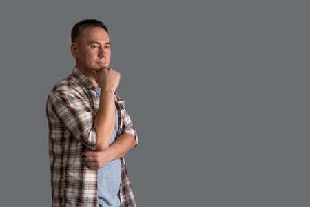 Portrait of a 30s man in casual clothes holding his hand on his chin on a gray background, copyspaceの写真素材
