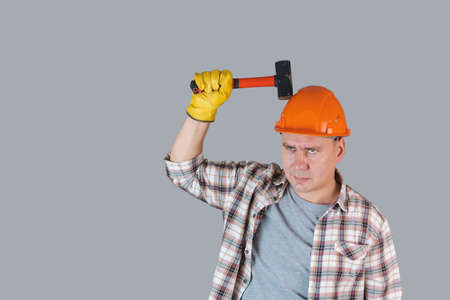 A worker in an orange hardhat hits a helmet with a hammer, protective workwear in industryの写真素材