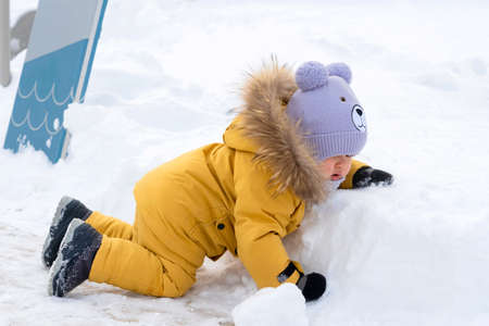 toddler 12-17 months old in yellow winter clothes slipped and fell on the snow