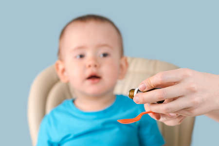 Mom pours the syrup with the medicine into a spoon, the toddler looks curiously at the spoon with vitamins.の写真素材