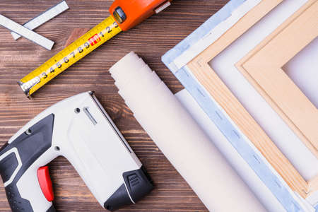 A tool for stretching canvas on a stretcher in the workshop. Forceps, tape measure, battery stapler for staples and finished paintings on canvas.の写真素材