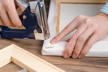 The artist stretches the canvas on a wooden stretcher, fixing the corner of the canvas with a stapler. top viewの写真素材