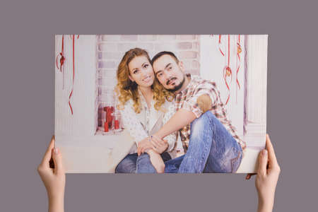 Women's hands hang a family photo printed on canvas framed in a stretcher on a gray wallの写真素材