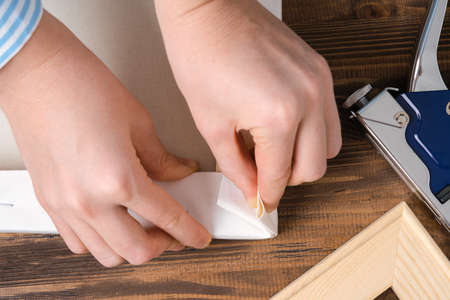 The artist stretches the canvas on a wooden stretcher, wrapping the canvas at the corner of the...