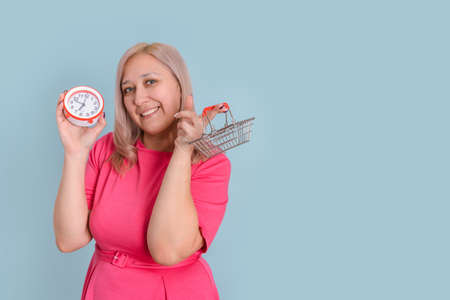 Cute blonde 40s adult woman with shopping bags and a small shopping basket on a blue background. copy spaceの写真素材