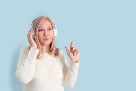 An adult woman in her 40s listens to music with wireless headphones and points her finger up while standing on a blue background. copy spaceの写真素材