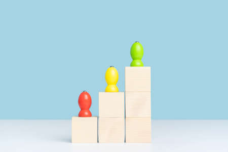 The concept of growth and development in business. Three wooden pawns stand on wooden cubes built in the form of a pyramid ladder.の写真素材
