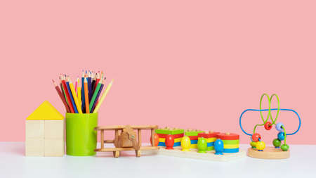A set of children's toys on a pink background. Wooden sorter, cubes, pencils and a maze with beads. The concept of eco-friendly toys made of wood.の写真素材