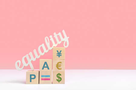 The concept of equal pay. The word equality stands on wooden cubes with dollar, euro and pound symbols. Copyspace on pink backgroundの写真素材