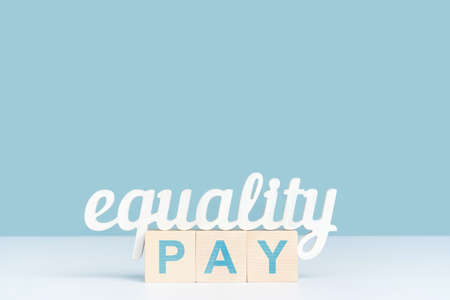 The concept of equal pay, the word equality stands on three wooden cubes with the inscription pay. Blue background, copy spaceの写真素材