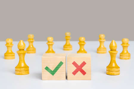 The concept of choice. A green check mark and a red cross on wooden cubes among chess pieces.