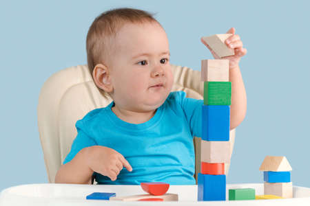 toddler 12-17 months is concentrating on building a tower of colorful wooden cubes sitting on a child's chair.の写真素材