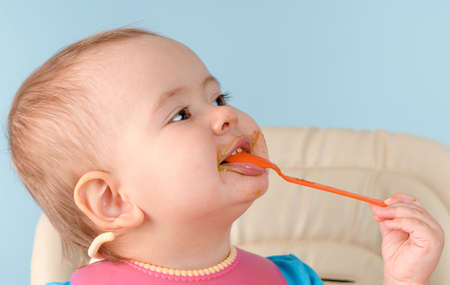 A happy smiling baby 12-17 months old eats broccoli vegetable puree with a spoonの写真素材