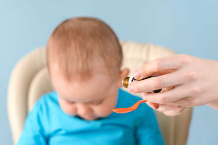Mom pours syrup with medicine into a spoon, toddler tilted his head and does not want to drink vitaminsの写真素材