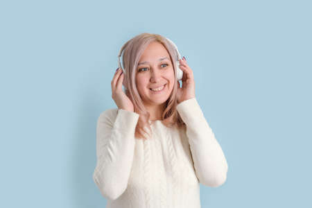 An adult woman in her 40s listens to music in wireless headphones standing on a blue background.の写真素材