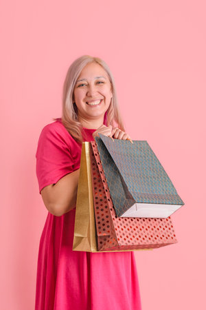 A 40-year-old adult woman holds a lot of shopping bags standing on a pink backgroundの写真素材