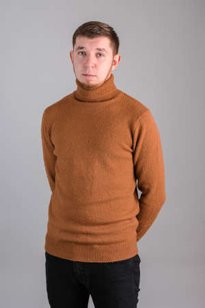 Portrait of a bearded man standing in a red sweater with his hands behind his back on a gray backgroundの写真素材