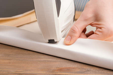 The artisan's hands pull the canvas onto a wooden stretcher with tongs and fasten it with a battery stapler. close-upの写真素材