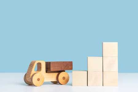 A wooden toy car stands next to a pyramid ladder made of wooden cubes on a blue background. The concept of logistics and cargo transportation.の写真素材
