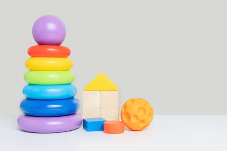 A set of children's educational toys on a gray background. A colored plastic pyramid of rings, wooden cubes and a rubber ball.の写真素材