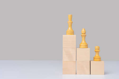 Wooden cubes arranged in the form of stairs and pyramids on which there are chess pieces in order of importance, pawn officer and queen. Mockup for a business concept, copy spaceの写真素材