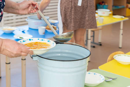 A kindergarten cook pours soup into a plate before lunch.の写真素材