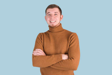Portrait of a bearded man smiling with his arms crossed standing on a blue backgroundの写真素材