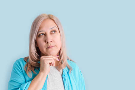 An adult woman was thinking with her hand under her chin standing on a blue background, copyspaceの写真素材