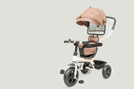 Beige children's tricycle with handle on gray background, copy spaceの写真素材