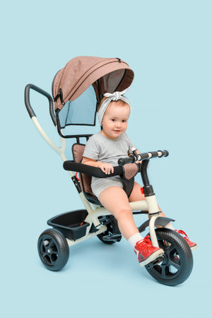 A happy child, a girl, is sitting on a tricycle, on a blue background.の写真素材