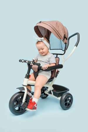 A cheerful little girl 2-3 years old is learning to ride a tricycle, on a blue background.の写真素材