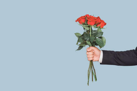 A man's hand with a bouquet of red roses on a blue backgroundの写真素材