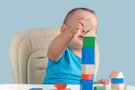 toddler 12-17 months building a tower of colorful wooden cubes sitting on a chair.の写真素材