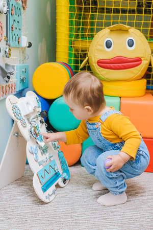 A little girl is playing with busy board in the playroomの写真素材