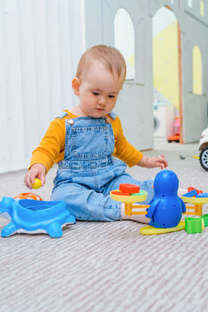 A small child is playing with toy scales sitting on the floor in the playroomの写真素材