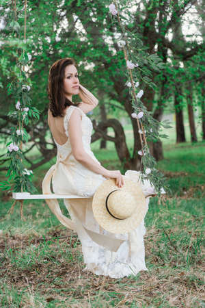 A girl in a dress is sitting on a rope swing in an apple orchard in springの写真素材