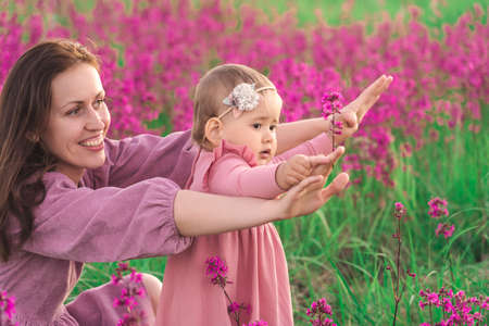 A happy mother with a child daughter aged two years have fun in a meadow with purple blooming flowersの写真素材