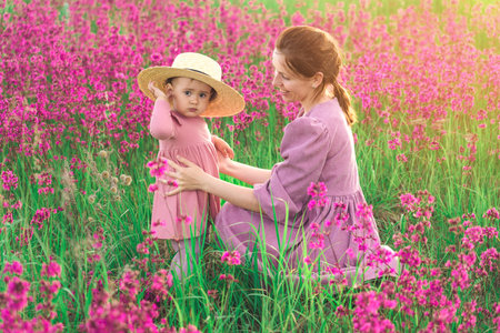 Happy family mother and baby daughter hug on meadow with blooming purple flowersの写真素材