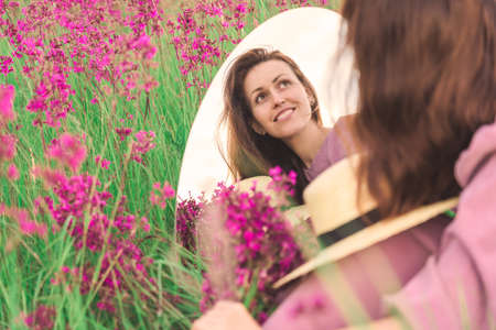 A portrait of a beautiful girl is reflected in a mirror in a meadow with purple wildflowersの写真素材