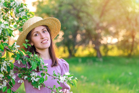 Portrait of a girl in a straw hat in a blooming apple orchard at sunset, copy-space