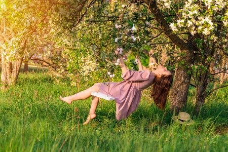 A brunette woman in a purple dress swings on a rope swing in an apple orchardの写真素材
