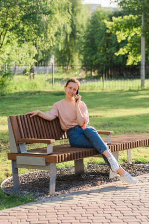 Beautiful brunette talking on the phone while sitting on a park benchの写真素材