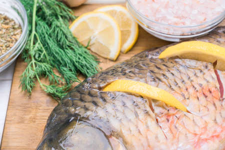 Raw carp fish stuffed with lemon slices lies on a cutting board, close-upの写真素材