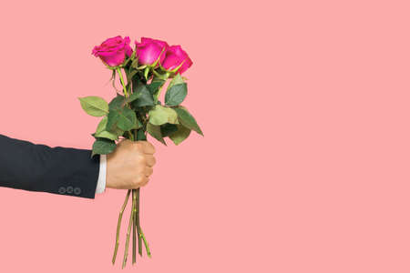 A man's hand holds out a bouquet of roses on a pink backgroundの写真素材
