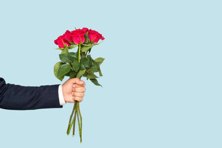A man's hand holds out a bouquet of roses on a blue backgroundの写真素材