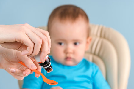 Mom pours vitamins into a spoon before giving them to a newborn baby sitting on a chair.の写真素材
