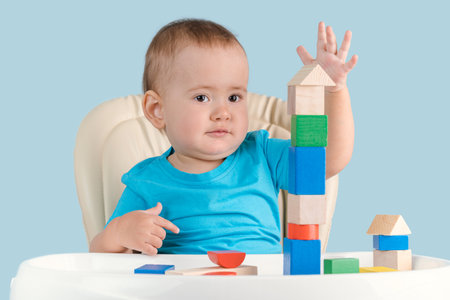 Joyful toddler 12-17 months old builds a tower of colorful wooden cubes sitting on a child's chair.の写真素材